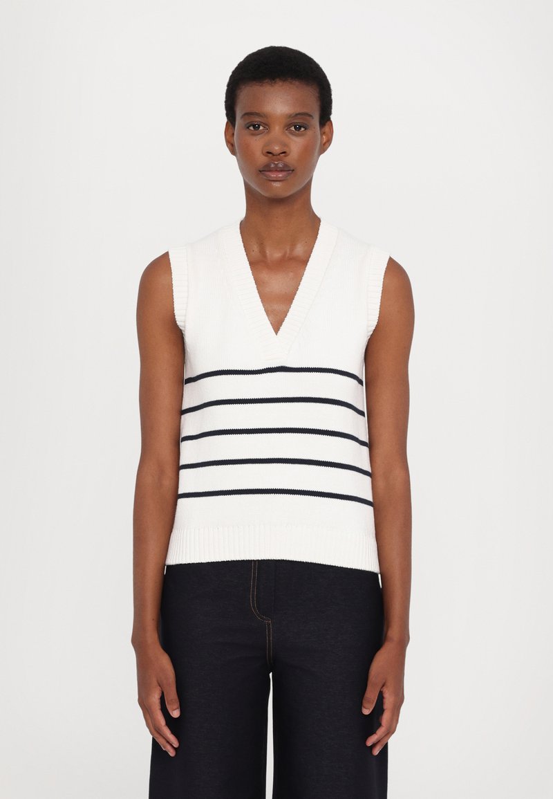 Débardeur en tricot blanc sans manches avec un décolleté en V, présentant des rayures horizontales bleu marine sur la poitrine. Ourlet et épaules côtelés.