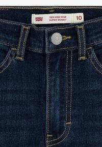 Jeans Levi's 720 de tiro alto super ajustados en denim azul oscuro. Presenta costuras visibles, un cierre frontal con botón y diseño de bolsillo estándar.