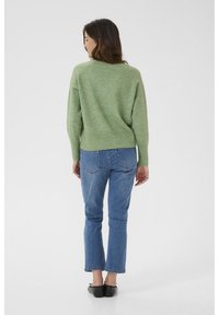 Pull en maille verte à coupe décontractée, associé à un jean bleu à coupe droite. La tenue est complétée par des ballerines noires simples et une texture nette et lisse.