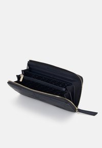 Portafoglio zip-around blu navy con molteplici scomparti, zip dorata e rivestimento interno con marchio, aperto su uno sfondo bianco.