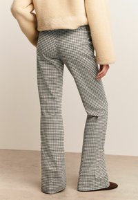 Un pantalon évasé à carreaux présente un motif noir et blanc, un tissu texturé, et une taille cintrée avec des coutures et des poches.