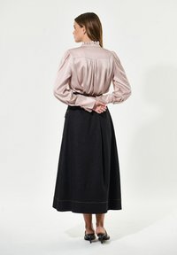 Seidige Bluse in Blush mit Rüschensaum, langen Puffärmeln; kombiniert mit einem langen, dunklen Jeansrock mit gelben Nähten.