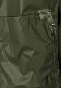 Giacca verde resistente all'acqua con una texture liscia, dotata di una tasca con cerniera prominente e leggere pieghe, progettata per l'uso all'aperto.