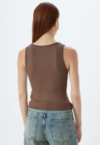 Bruine geribbelde mouwloze top met een ronde hals, slim fit ontwerp en subtiele textuur, gecombineerd met lichtblauwe denim jeans.