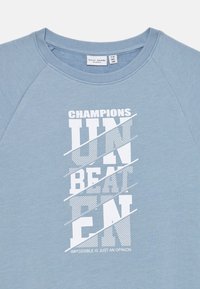Un sweat-shirt bleu clair en tissu doux, avec un texte blanc audacieux. Le design comprend des lignes diagonales et une mise en page graphique avec un slogan en bas.