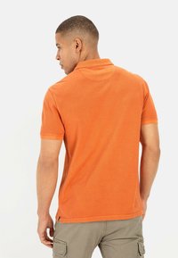 Oranje katoenen polo shirt met korte mouwen, een kraag en zijsplitten aan de onderkant. Het ontwerp heeft een gladde textuur en een klassieke snit.