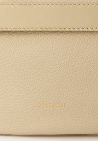 Μπεζ δερμάτινο πορτοφόλι με υφή, διακοσμημένο με διακριτική ραφή και ανάγλυφο χρυσό λογότυπο. Συμπαγές ορθογώνιο σχήμα.