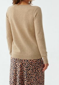 Maglione beige a maglia con maniche lunghe, polsini e orlo a coste, indossato sopra una gonna a fiori nei toni del blu navy, pesca e crema.