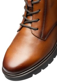 Brun læderstøvle med mørkegrå snørebånd, detaljeret syning og en tyk sort gummisål.