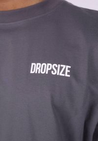 Tricou din bumbac gri, cu guler rotund și un logo alb imprimat "DROPSIZE" pe piept. Textură netedă, fără modele.