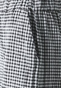 Tissu vichy noir et blanc avec une texture froissée, présentant des coutures froncées et une coupe ample, mettant en avant un motif à carreaux classique.