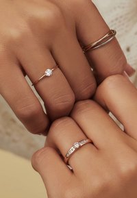 Drie ringen aan de vingers: een dunne rosegouden band met een enkele diamant, een gedraaide gouden band en een rosegouden ring met kleine ingelegde diamanten.