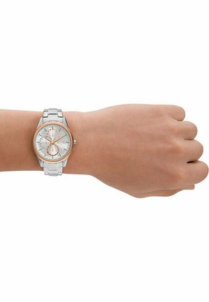 Silberne und roségoldene Uhr am Handgelenk, mit einem runden Zifferblatt, drei Hilfszifferblättern und einem Metallarmband mit einer polierten, gebürsteten Oberfläche.
