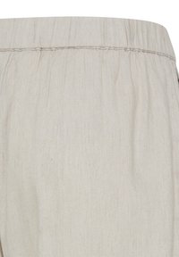 Ceinture élastique beige avec tissu froncé, montrant la texture et les détails des coutures sur un tissu léger tissé.
