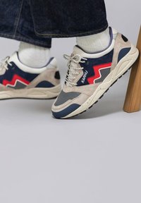 Sneakers con tomaia in suede grigio e mesh blu navy, accenti zigzag rossi, lacci maculati e suola in gomma testurizzata.