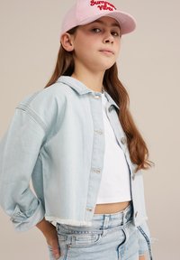 Light blue denim jacket with frayed hem, featuring silver buttons. Worn over a white top, paired with distressed light blue jeans and a pink cap.