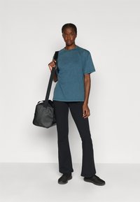 Mėlynos spalvos medvilninė marškinėliai su trumpomis rankovėmis, derinami su juodomis plačiomis kelnėmis ir juodais sportiniais bateliais. Nešiojama juoda petneša.