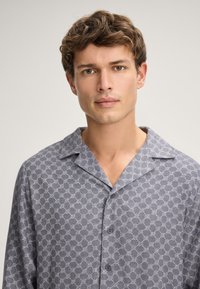 Short-sleeve, collared shirt in patterned gray fabric, features a subtle geometric design and button closure. Soft, lightweight texture.
