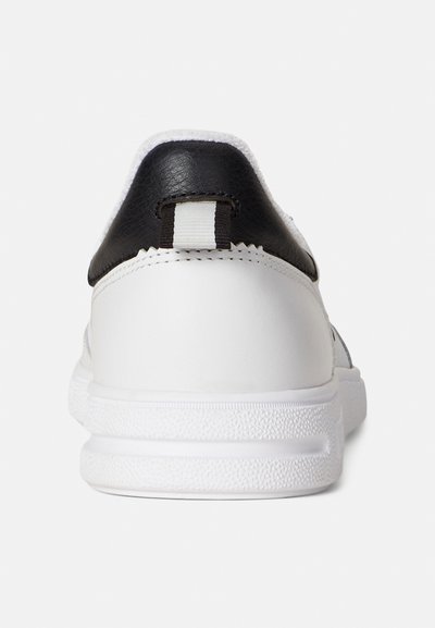 White sneakers with a smooth texture, black leather heel, and a contrasting white tab on the back. Rubber outsoles with a textured grip.