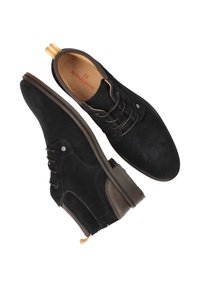 Zwarte suède schoenen met een ronde neus, bruine accenten, vetersluiting en een gestructureerd zijpaneel. Beschikt over een lusvormige aantrekband.