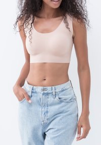 Beige sømløs bralette med brede stropper og rund udskæring, parret med højtaljede lyseblå denim jeans.