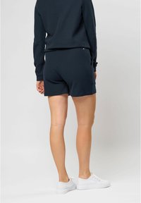 Námořnické modré šortky s texturovanou tkaninou, s přiléhavým střihem. V kombinaci s bílými teniskami, což vytváří ležérní a pohodlný vzhled.