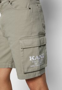 Shorts cargo beiges en coton. Dotés d'une grande poche latérale et d'un logo brodé. Tissu texturé avec des détails de couture visibles.
