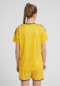 Gul atletisk tröja och shorts, tillverkade av lätt material. Har svarta detaljer på axlarna, korta ärmar och rund halsringning.