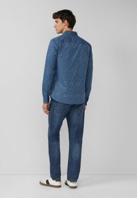 Niebieska koszula w wzory z długim rękawem i kołnierzem typu spread, zestawiona z niebieskimi dżinsami i białymi trampkami z ciemnymi akcentami.