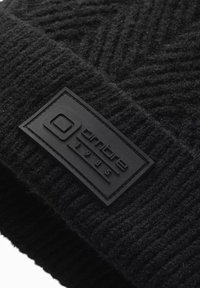 Black knitted beanie featuring a textured pattern and a rectangular black rubber label embossed with "ombre" and "1985."