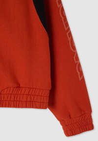 Manica e vita di felpa rossa con polsini elasticizzati e un sottile dettaglio in rilievo sulla manica.