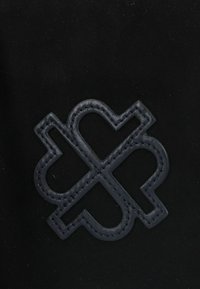 Tessuto nero con un logo goffrato di un blu navy scuro in un design geometrico, con cuciture a contrasto che delineano la forma del logo.