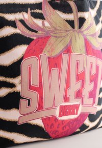 Geantă din material textil multicolor cu un grafic mare cu o căpșună roz și textul „SWEET BERRY”. Fundalul prezintă un model de zebre în negru și bej.