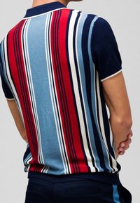 Stickad polotröja med vertikala ränder i röd, blå och marinblå, med ribbad krage och korta ärmar. Slät textur och figurnära design.