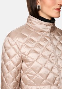 Leichte, gepolsterte Jacke in hellrosa mit einem Rautenmuster. Verfügt über einen Stehkragen und Druckknöpfe entlang der Vorderseite.