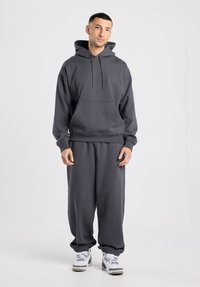 Grijze hoodie met capuchon en een zak aan de voorkant, gecombineerd met loszittende grijze joggingbroek met elastische boorden en bijpassende sneakers.