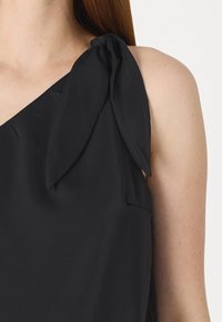 Fekete ujjatlan felső aszimmetrikus dizájnnal, egyik vállán masnis részlettel és sima textil felülettel.