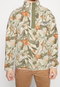 Pullover in pile con motivo floreale astratto nei toni del verde e dell'arancione, dotato di un collo alto, bottoni a scatto e una tasca laterale con zip.