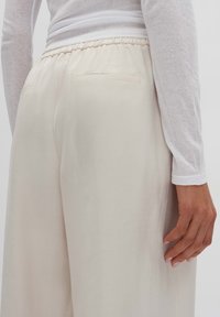 Beige wide-leg trousers with an elastic waistband, featuring two back pockets and a smooth, lightweight fabric texture.