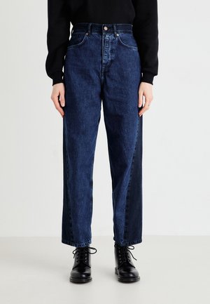 Person trägt hochgeschnittene, zweifarbige dunkelblaue Jeans kombiniert mit schwarzen Schnürstiefeletten und einem schwarzen Langarmshirt.