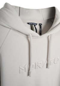 Sudadera con capucha de color gris claro que presenta un acabado texturizado, logotipo en relieve y cordones. La etiqueta indica un diseño de corte cuadrado.