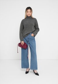 Pulover gri cu guler înalt, asortat cu blugi largi de culoare albastră, ținând o geantă cu șnur bordeaux; pantofii cu vârf ascuțit de culoare neagră completează ținuta.