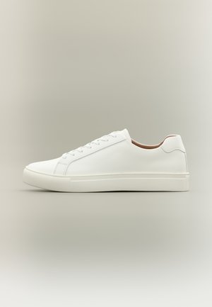 Zapatilla blanca de corte bajo con cierre de cordones y suela plana, mostrada de perfil sobre un fondo neutro.