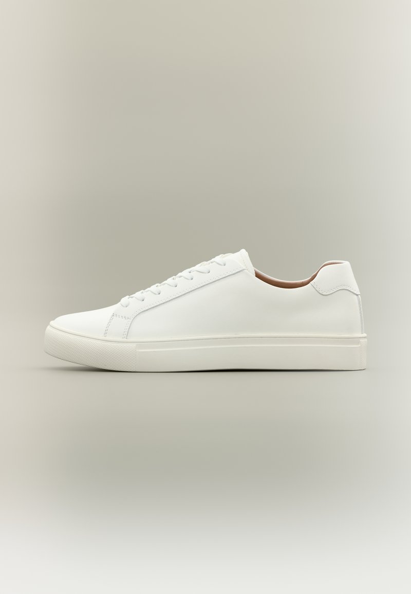 Άσπ ρο sneaker χαμηλού προφίλ με κλείσιμο κορδονιών και επίπεδη σόλα, εμφανιζόμενο από το πλάι σε ουδέτερο φόντο.