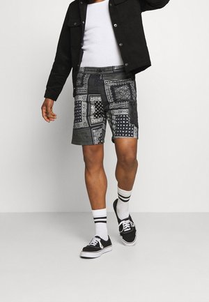 Black patchwork shorts featuring varied denim patterns, textured fabric, and a relaxed fit, paired with black sneakers and striped socks.