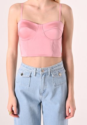 Kvinde iført lyserød cropped bustier-top med tynde stropper kombineret med højtaljede lyseblå jeans med tekstureret linning og klaplommer.