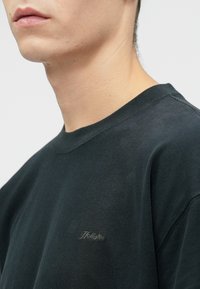 Σκούρο γκρι βαμβακερό μπλουζάκι με στρογγυλή λαιμόκοψη και κοντά μανίκια, με διακριτό λογότυπο "Hollister" κεντημένο στο αριστερό στήθος.