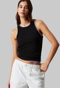 Top nero senza maniche con texture a coste e scollatura di un viola chiaro a contrasto, abbinato a pantaloni a righe chiare con etichetta logo.