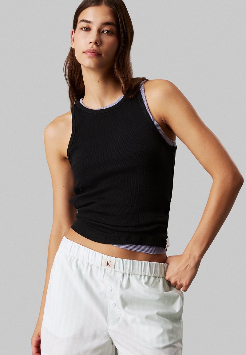 Top nero senza maniche con texture a coste e scollatura di un viola chiaro a contrasto, abbinato a pantaloni a righe chiare con etichetta logo.