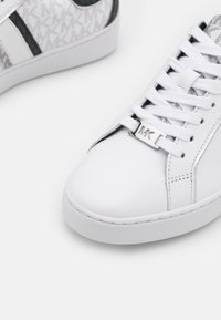 Białe skórzane sneakersy z teksturowanym szarym akcentem, z logo MK w kolorze srebrnym w okolicy sznurowania oraz klasycznym okrągłym noskiem.